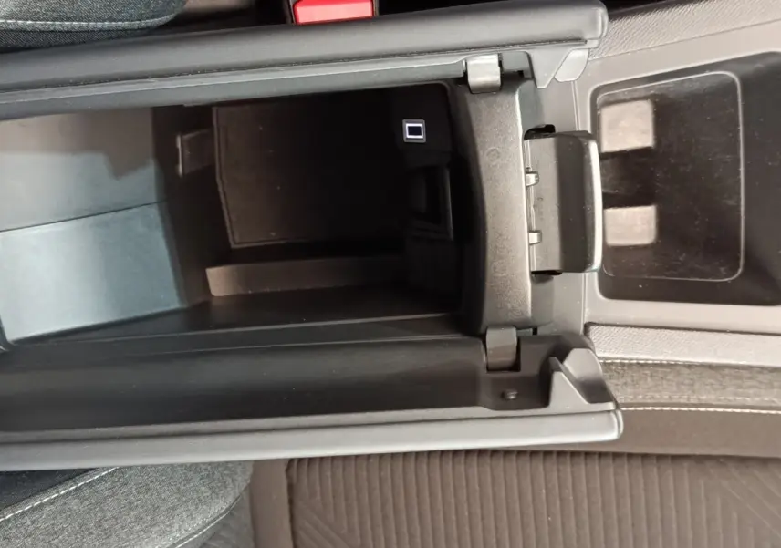 Vue plongeante sur le rangement central noir ouvert de la Peugeot 308 2023 essence, avec console et siège tissu gris.