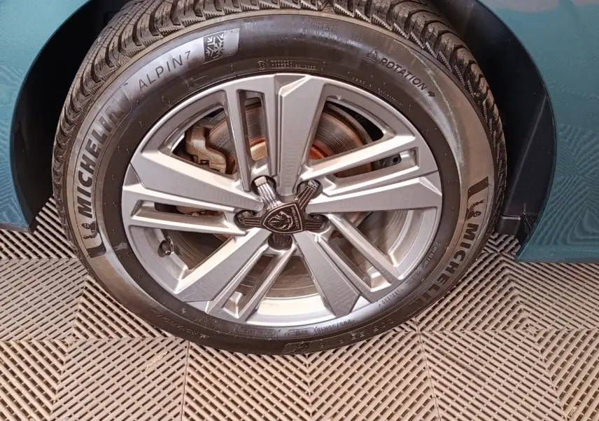 Gros plan sur la roue avant gauche d'une Peugeot 308 2023 bleu vert avec jante alliage et pneu Michelin Alpin 7.