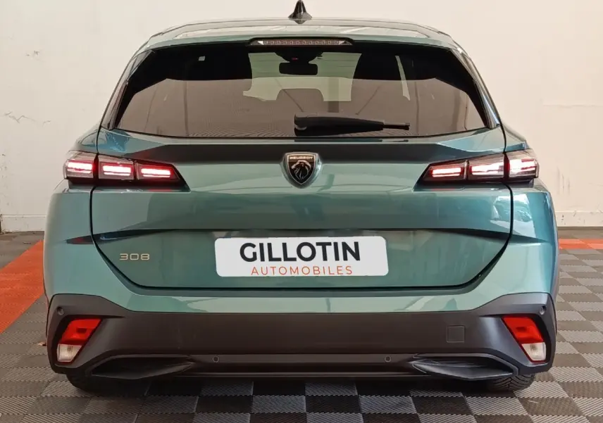 Vue arrière d'une Peugeot 308 2023 vert métallisé avec feux LED allumés et logo lion central sur hayon.