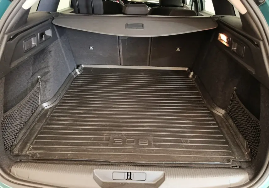 Vue intérieure du coffre noir d'une Peugeot 308 2023 avec tapis de protection et filets latéraux de rangement.