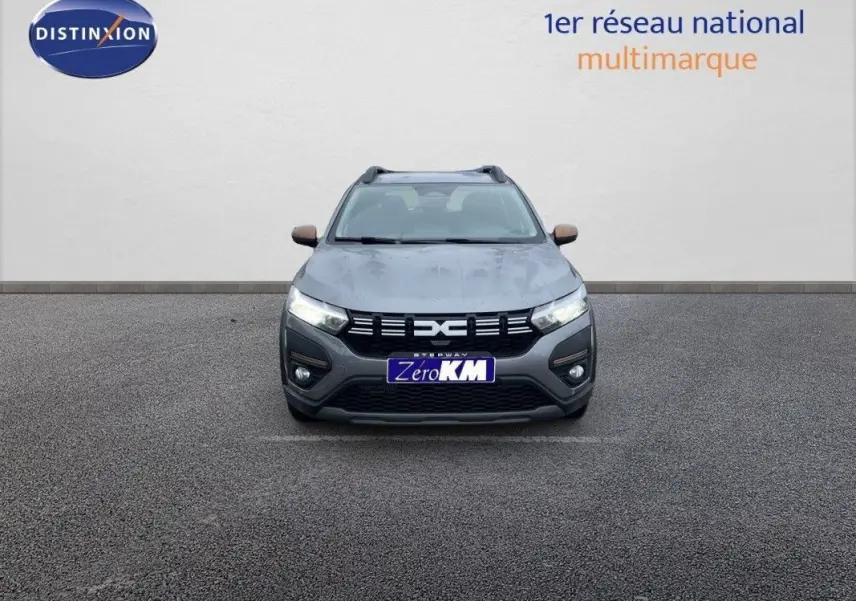 Vue frontale d'une Dacia Sandero Stepway gris schiste métal avec calandre noire et feux allumés sur fond neutre.