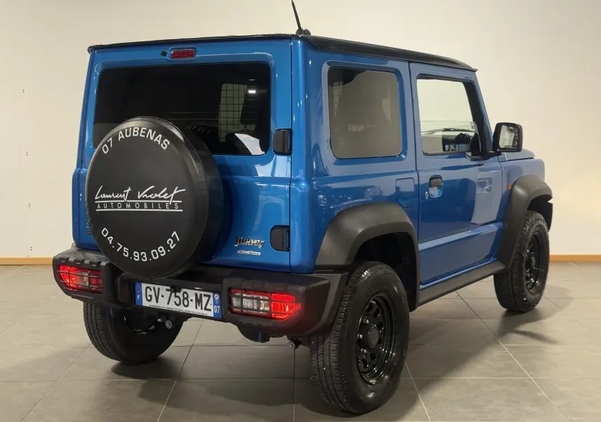 Vue 3/4 arrière droite d'un Suzuki Jimny bleu 2021 avec roue de secours noire et protections d'ailes noires.