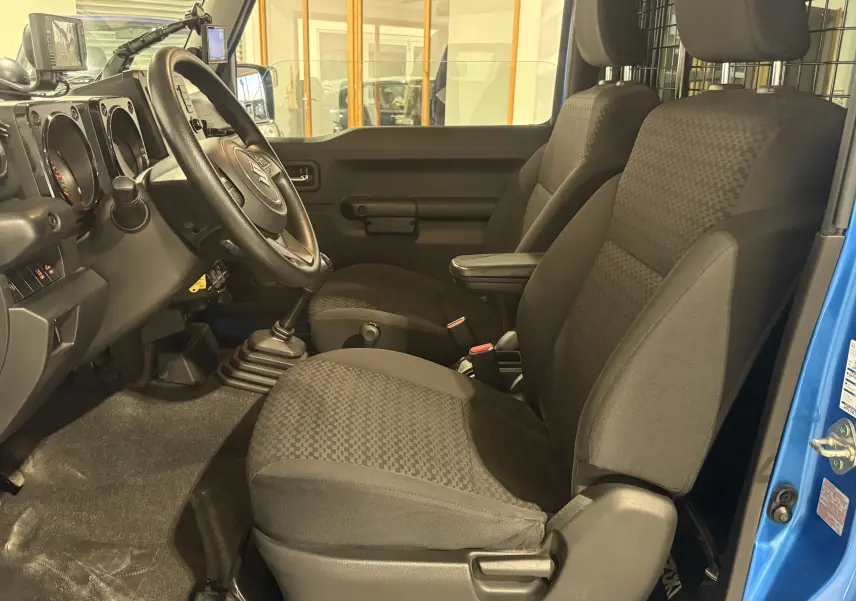 Intérieur du Suzuki Jimny 2021 bleu, vue côté conducteur montrant les sièges noirs et la boîte manuelle.