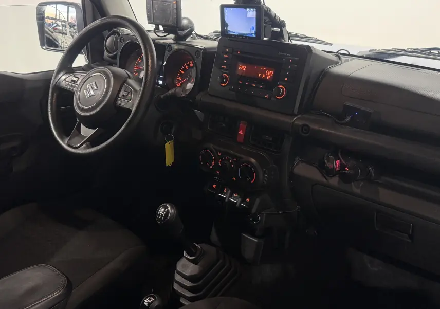 Vue intérieure côté conducteur du Suzuki Jimny 1.5 VVT Privilège 2021, avec tableau de bord noir et levier de vitesses manuel.