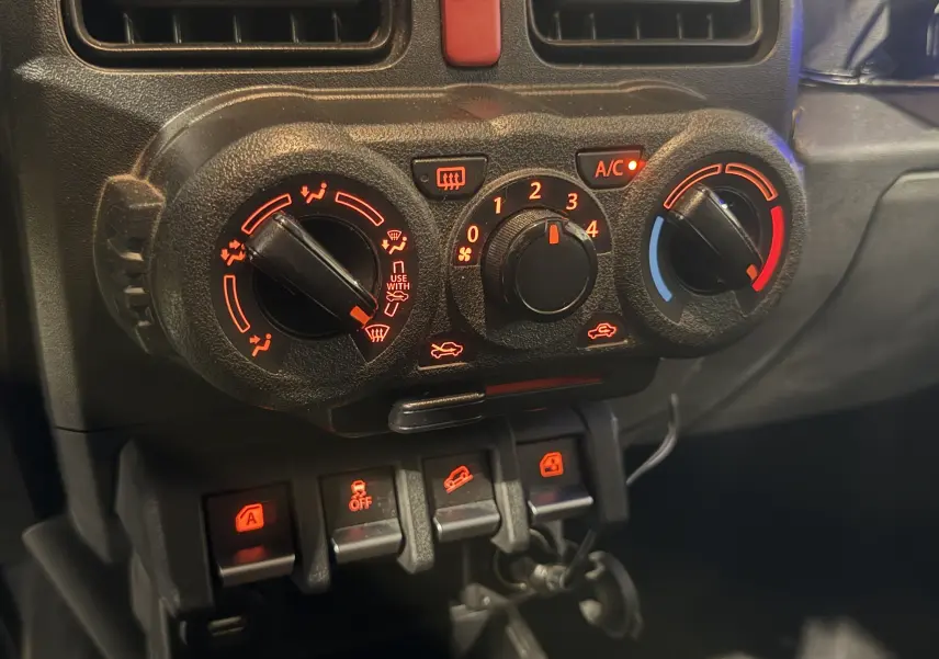 Gros plan sur les commandes de climatisation et les boutons de fonction du tableau de bord du Suzuki Jimny bleu 2021.