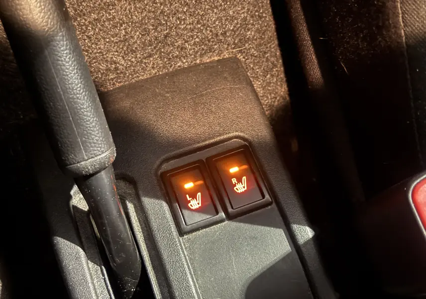Gros plan sur les boutons de chauffage des sièges avant allumés dans un Suzuki Jimny bleu 2021, version Privilège Allgrip.