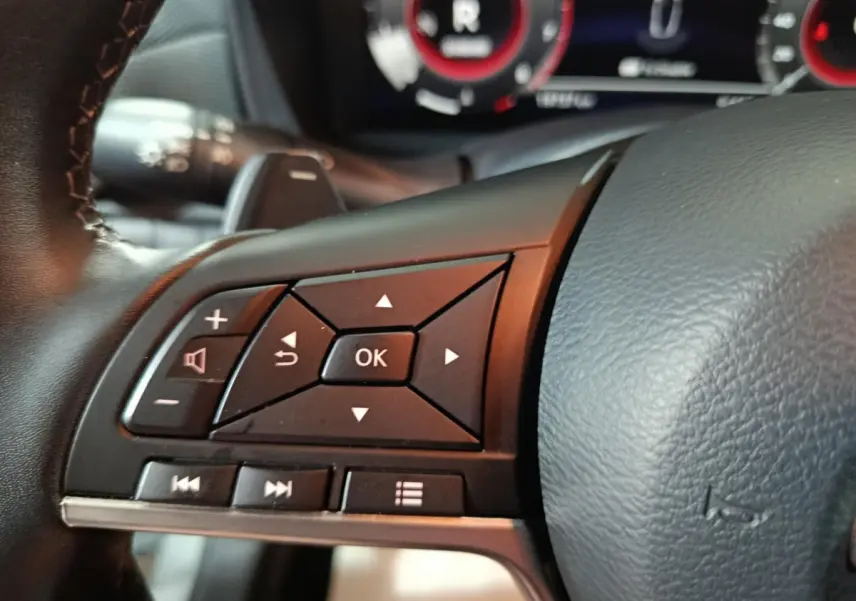 Gros plan sur les commandes multifonctions noires à gauche du volant cuir d'un Nissan Juke gris foncé 2025.