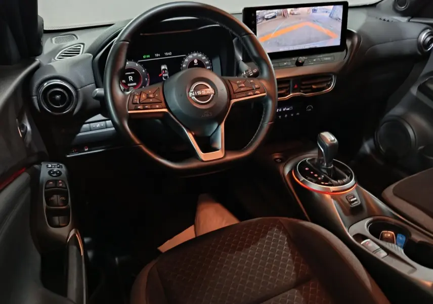 Intérieur du Nissan Juke gris foncé, vue du poste de conduite avec volant multifonction et écran tactile central affichant la caméra de recul.
