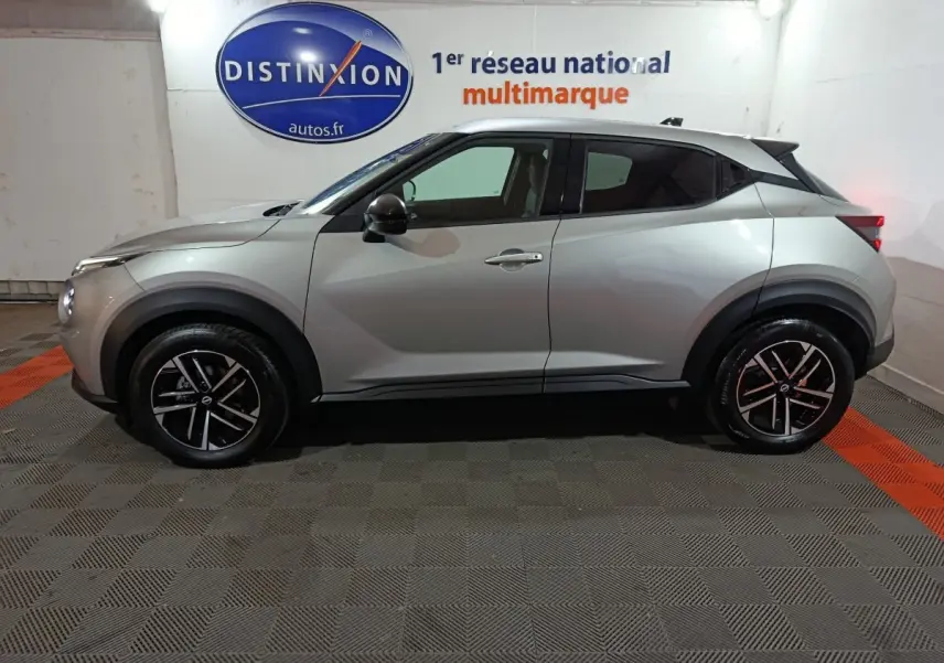 Vue de profil côté gauche d'un Nissan Juke gris foncé avec jantes noires et toit blanc dans un showroom.