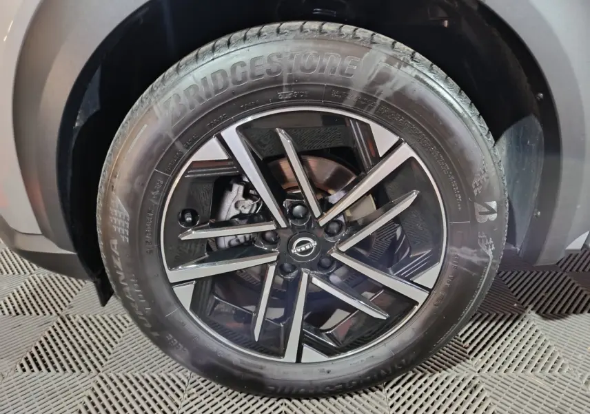 Gros plan sur la roue avant droite du Nissan Juke gris foncé, jante alliage noire à design moderne.