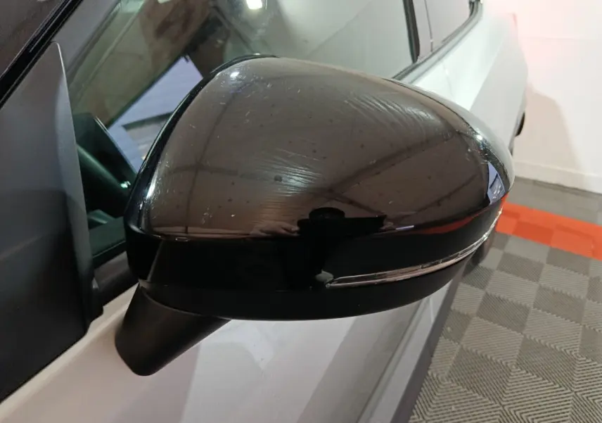 Gros plan sur le rétroviseur droit noir brillant du Nissan Juke gris foncé, avec clignotant intégré visible.