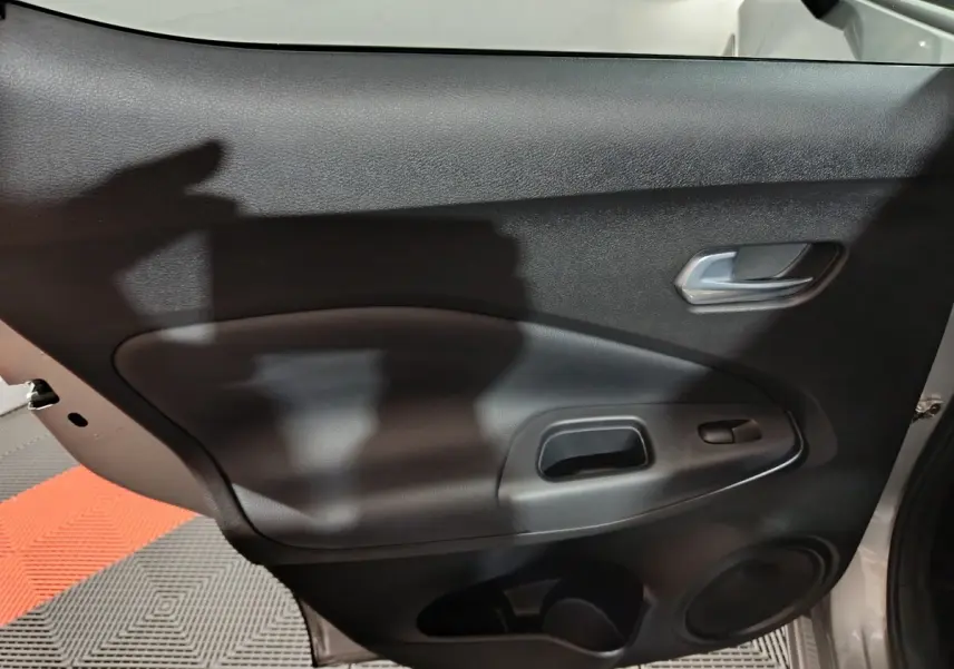 Gros plan sur la porte intérieure côté droit du Nissan Juke gris foncé, montrant la poignée et les commandes de fenêtre.