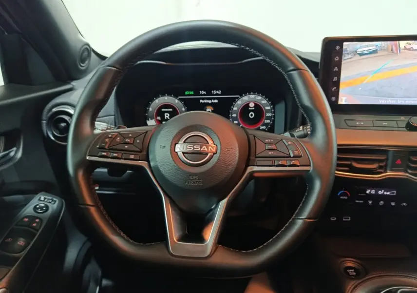 Vue intérieure centrée sur le volant noir du Nissan Juke 2025 avec tableau de bord numérique et écran tactile latéral.