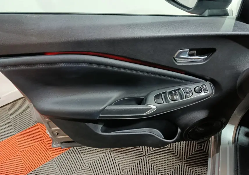 Vue rapprochée de la porte avant gauche intérieure du Nissan Juke gris foncé, avec commandes de vitres et rétroviseur.