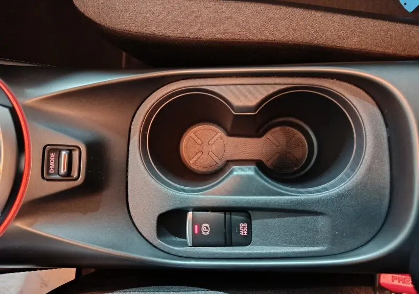 Vue plongeante sur la console centrale du Nissan Juke gris foncé, avec porte-gobelets et frein à main électrique.