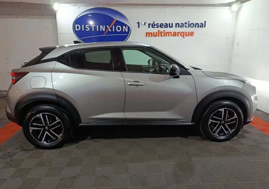Vue de profil côté gauche d'un Nissan Juke gris foncé 2025 avec jantes noires et détails noirs contrastants.