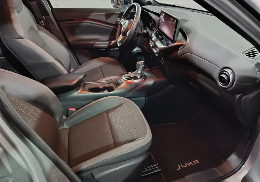Vue intérieure côté passager du Nissan Juke gris foncé 2025, avec tableau de bord moderne et écran tactile central.