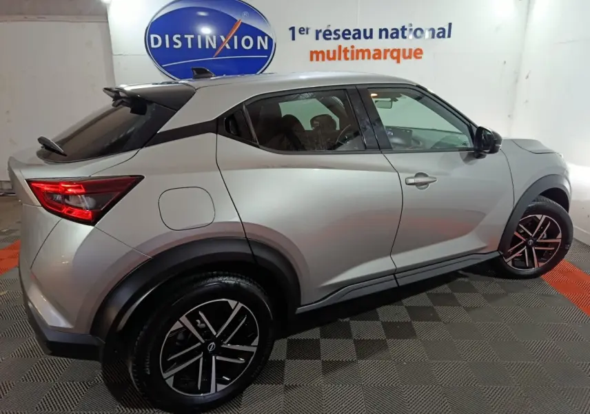 Vue latérale droite du Nissan Juke gris foncé 2025 avec jantes noires et toit noir contrasté dans un showroom.