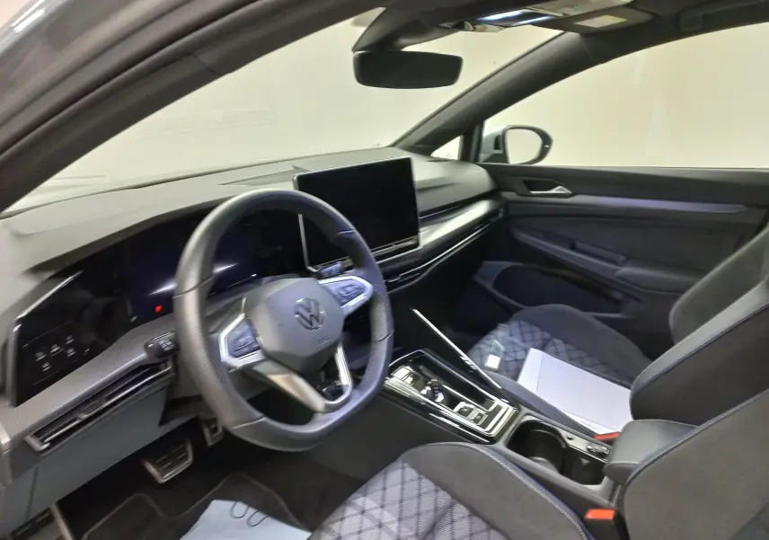 Vue intérieure côté conducteur de la Volkswagen Golf 1.5 eTSI R-Line 2025, avec tableau de bord numérique et écran central tactile.
