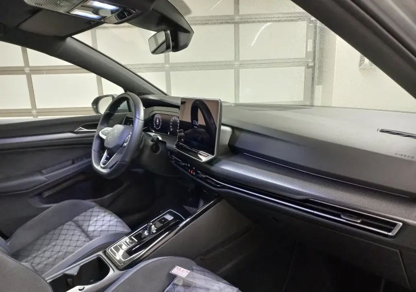 Vue intérieure côté conducteur de la Volkswagen Golf 1.5 eTSI R-Line 2025 avec tableau de bord noir et écran tactile central.