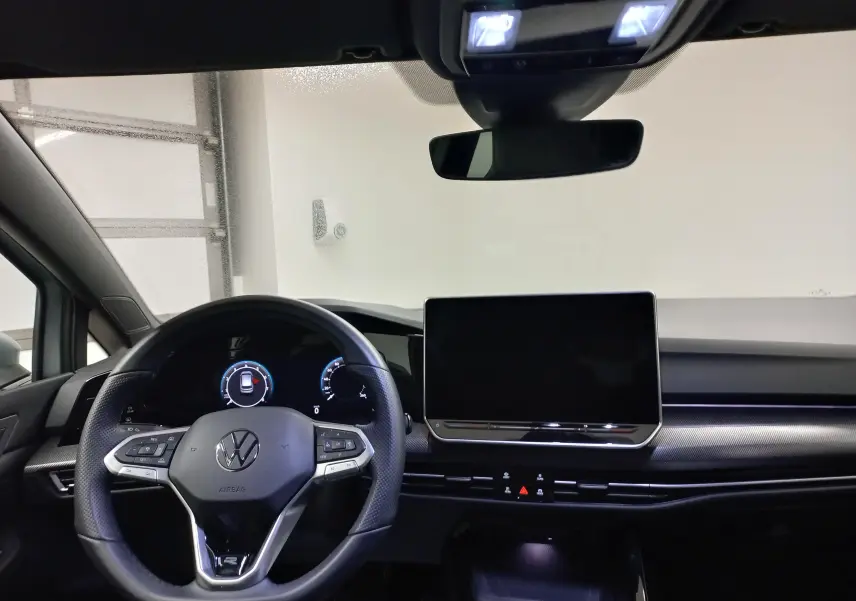 Vue intérieure frontale du tableau de bord de la Volkswagen Golf 1.5 eTSI R-Line avec écran tactile et volant multifonction noir.