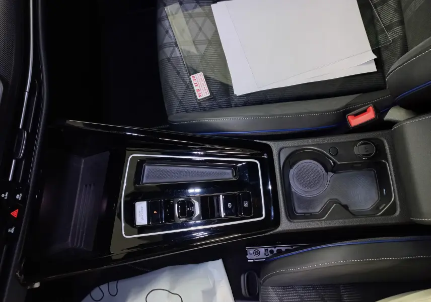 Vue plongeante sur la console centrale noire brillante de la Volkswagen Golf 1.5 eTSI R-Line avec sièges tissu gris et surpiqûres bleues.