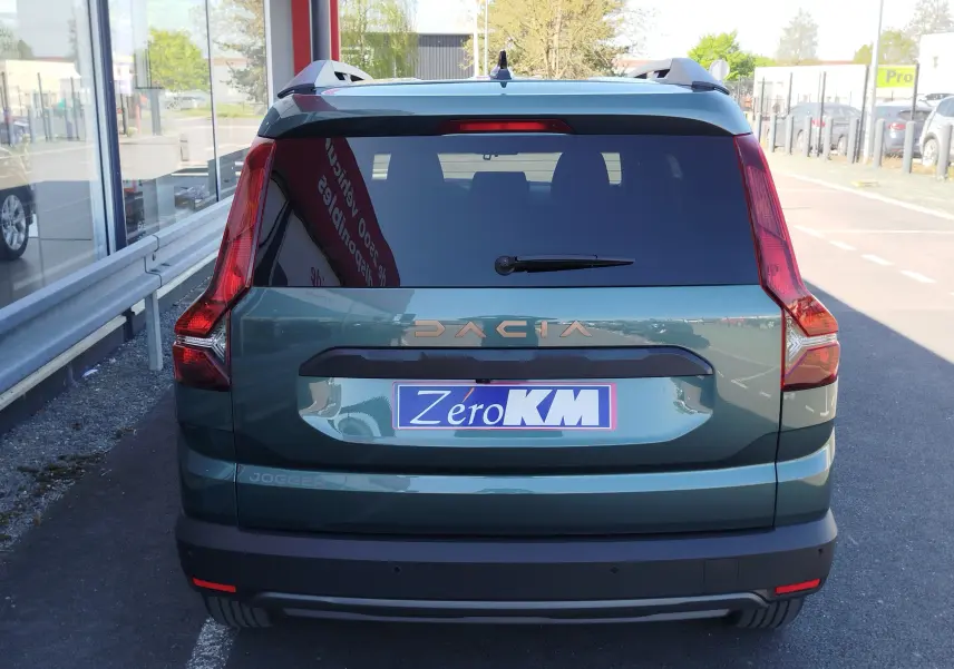 Vue arrière d'un Dacia Jogger vert cèdre métal 2026 avec logo Dacia en relief cuivré et plaque Zéro KM.