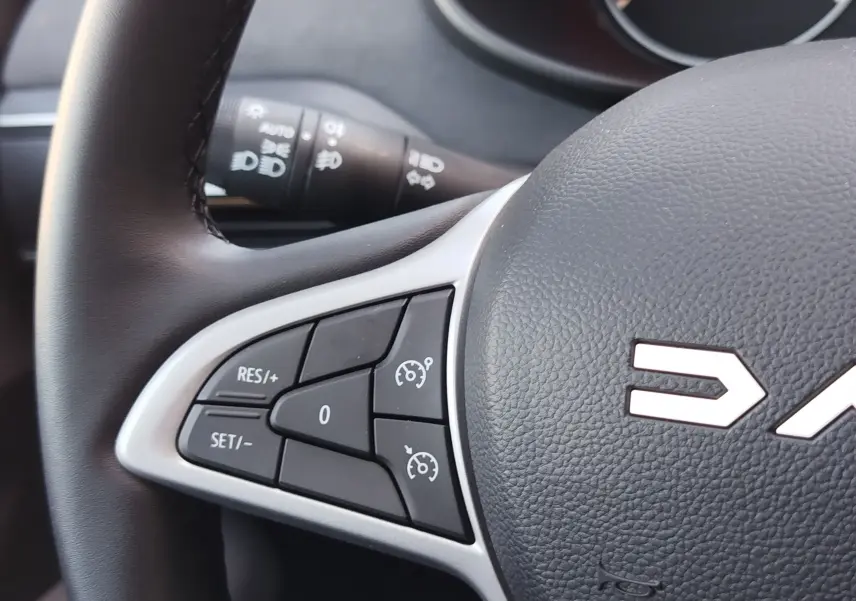 Gros plan sur les commandes de régulateur de vitesse au volant noir du Dacia Jogger 2026, intérieur sobre.