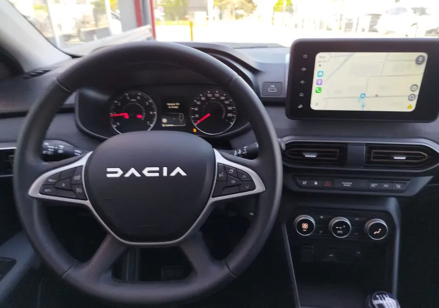 Vue intérieure centrée sur le volant noir DACIA et le tableau de bord avec écran tactile affichant la navigation.