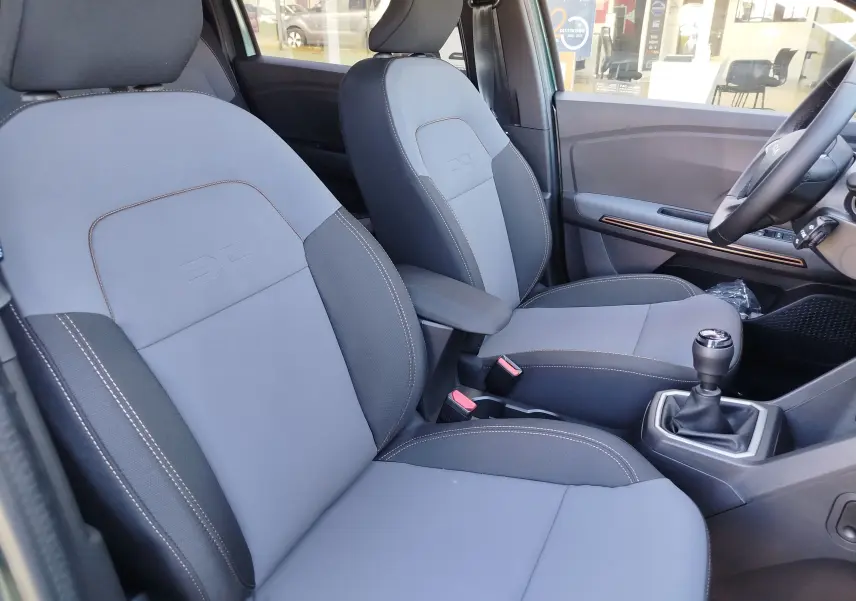 Vue intérieure côté conducteur du Dacia Jogger 2026, sièges tissu gris avec surpiqûres contrastées et levier de vitesse manuel.