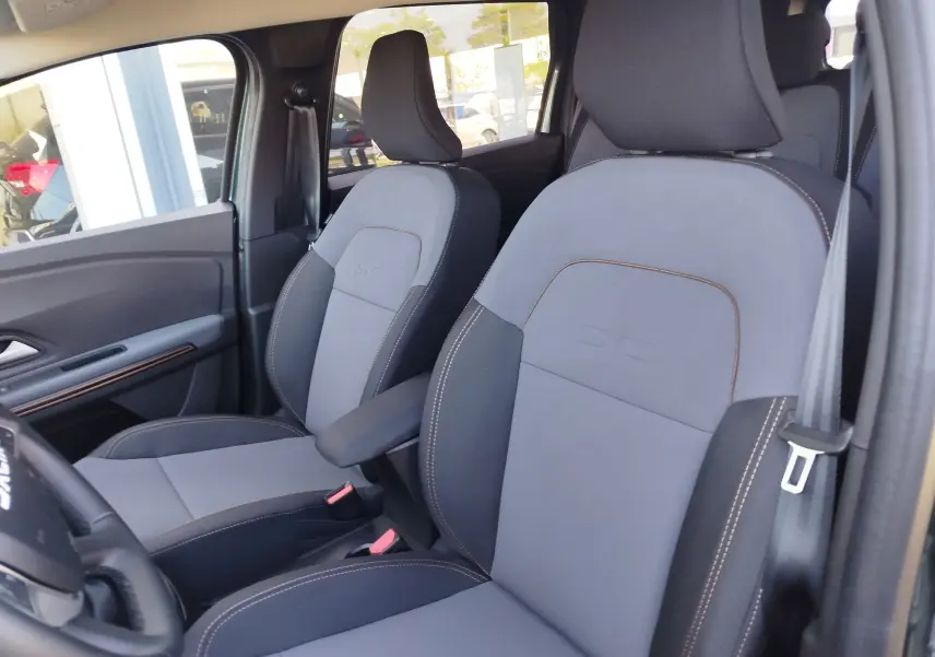 Vue intérieure côté avant droit du Dacia Jogger 2026, sièges tissu gris avec surpiqûres contrastantes et logo SC embossé.