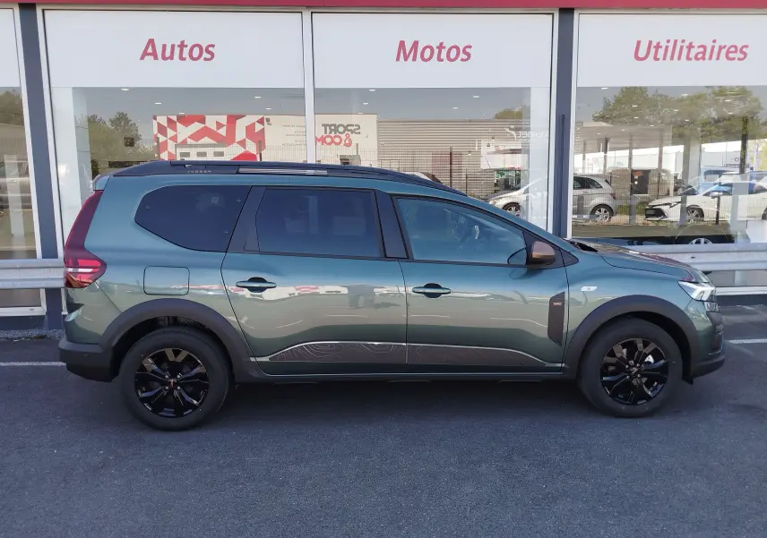 Profil latéral droit d'un Dacia Jogger 1.0 ECO-G 100CH EXTREME 7 places en vert cèdre métal avec jantes noires et stickers décoratifs.