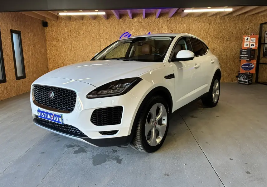 Jaguar E-PACE blanc en 3/4 avant droit dans un garage, avec calandre noire et jantes argentées.