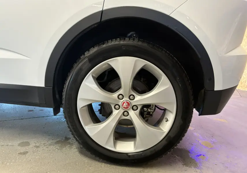 Gros plan sur la roue arrière droite blanche d’un Jaguar E-PACE 2.0D 180 R-DYNAMIC HSE avec jante argentée et logo Jaguar central.