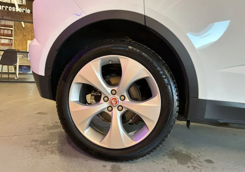 Gros plan sur la roue avant gauche d’un Jaguar E-PACE blanc, mettant en valeur la jante argentée et le logo Jaguar central.
