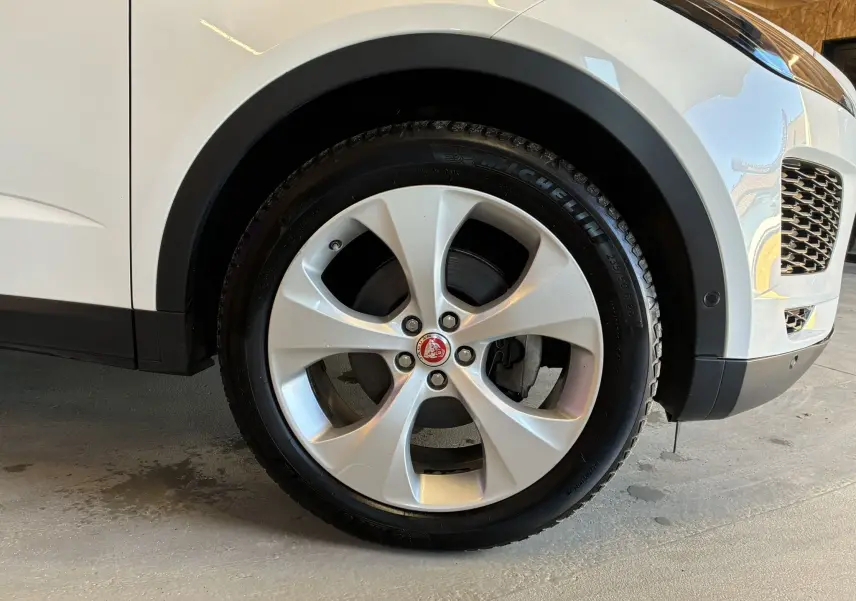 Gros plan sur la roue avant droite du Jaguar E-PACE blanc, mettant en valeur la jante argentée et le logo Jaguar central.