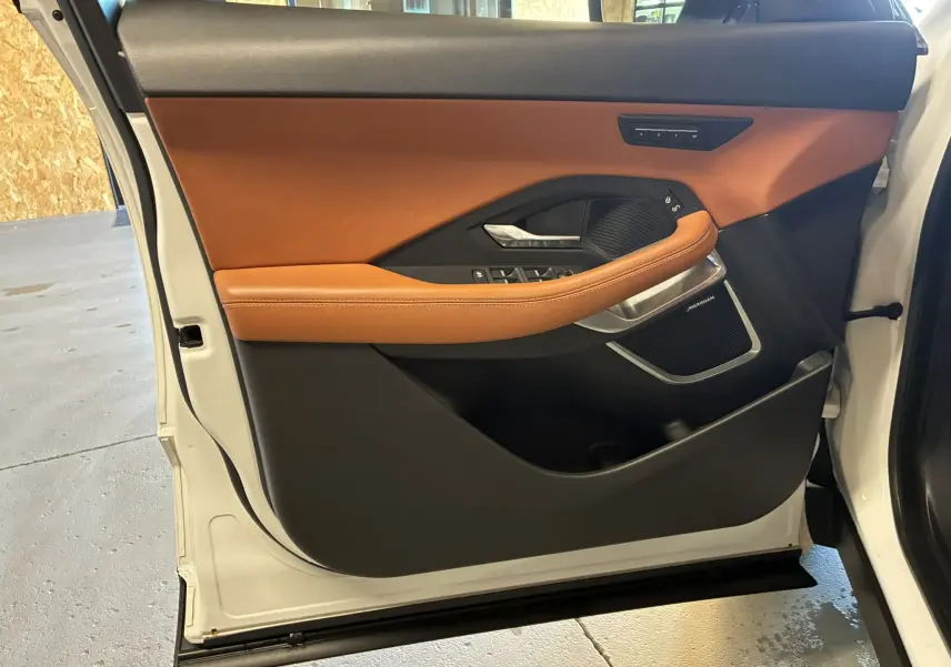 Vue intérieure de la porte avant gauche du Jaguar E-PACE blanc 2019 avec garniture cuir brun et commandes intégrées.
