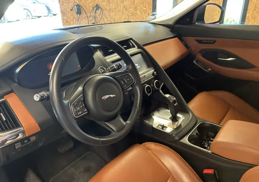 Vue intérieure côté conducteur du Jaguar E-PACE 2019, mettant en valeur le volant noir et les sièges en cuir brun.