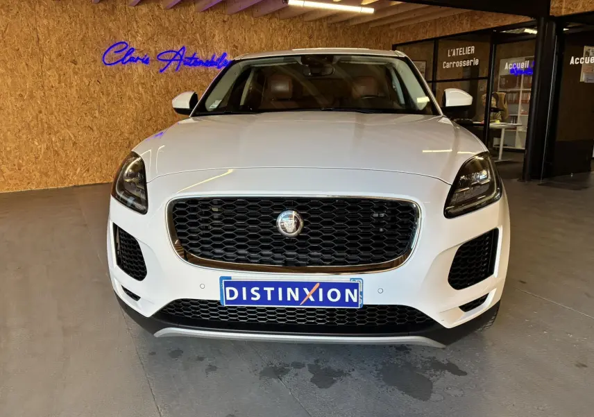 Vue frontale d'un Jaguar E-PACE blanc 2019 avec calandre noire et intérieur cuir brun visible en showroom.