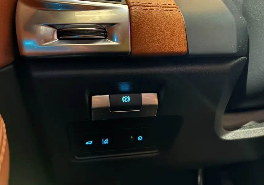 Détail intérieur du Jaguar E-PACE 2019 montrant les commandes électroniques de frein à main et ouverture du coffre, avec cuir brun.