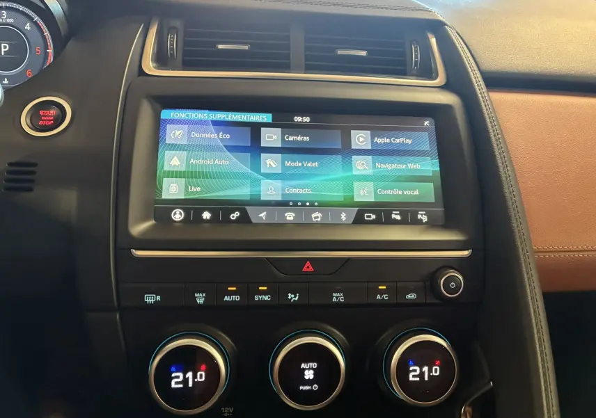 Vue rapprochée du tableau de bord du Jaguar E-PACE blanc 2019, avec écran tactile et commandes de climatisation visibles.