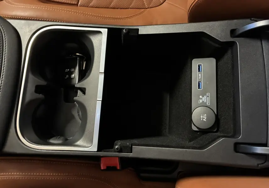 Vue rapprochée de la console centrale du Jaguar E-PACE blanc 2019, avec porte-gobelets, prise 12V et ports USB.