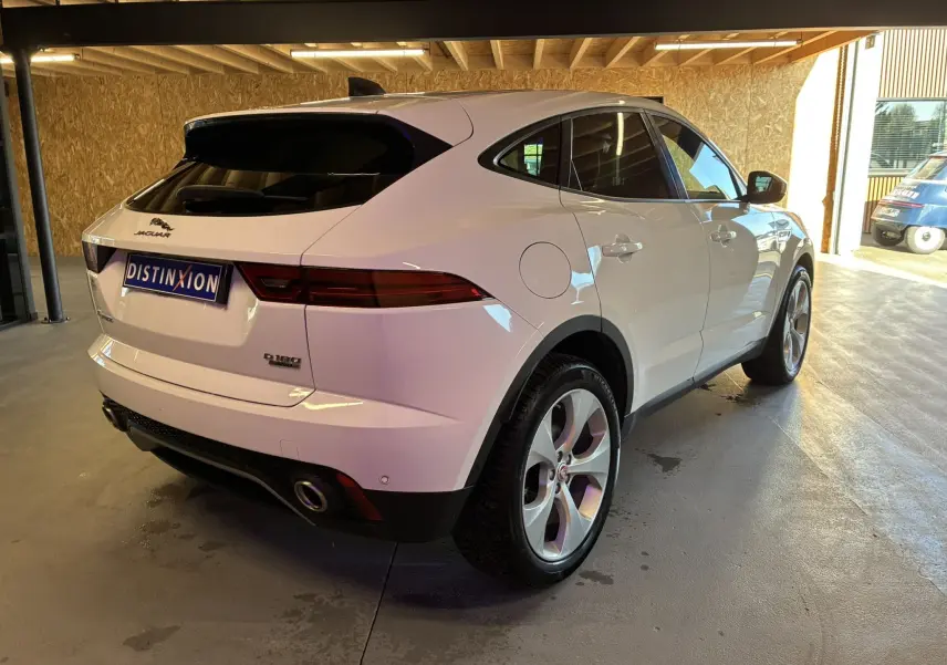Jaguar E-PACE blanc vue 3/4 arrière droit dans un garage, avec feux arrière allongés et jantes argentées.