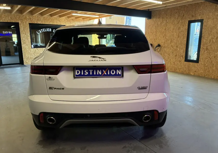 Vue arrière d'un Jaguar E-PACE blanc 2019 dans un garage, avec double sortie d'échappement et logo distinctif.
