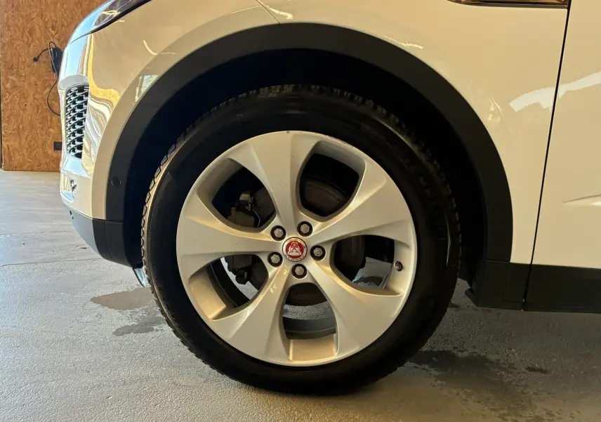 Gros plan sur la roue avant gauche d’un Jaguar E-PACE blanc, mettant en valeur la jante argentée et le logo central rouge.