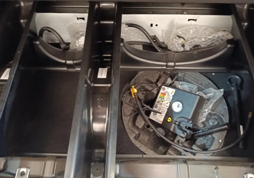 Compartiment de rangement sous le plancher du coffre de la Renault ZOE blanche, avec kit de gonflage visible.