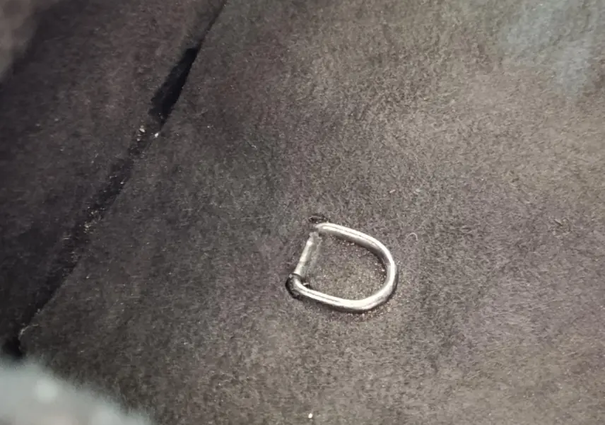 Détail d'un anneau d'attache métallique fixé sur la moquette noire du coffre d'une Renault ZOE blanche.