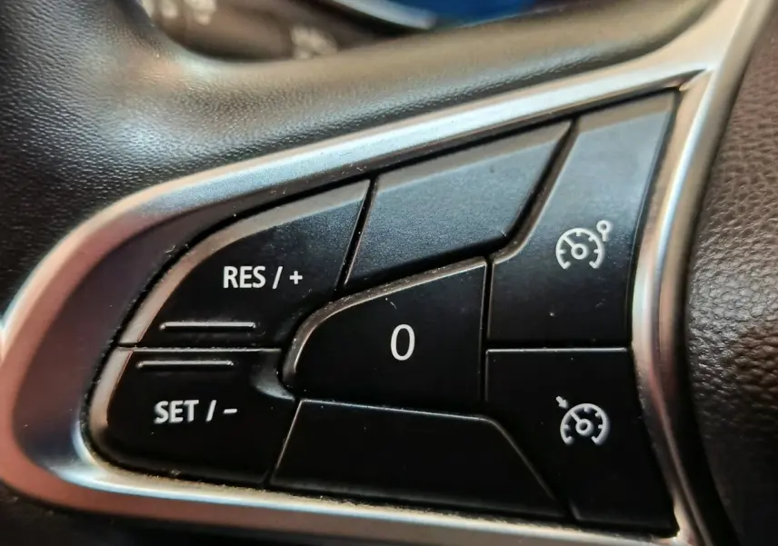 Gros plan sur les commandes du régulateur de vitesse au volant cuir synthétique d'une Renault ZOE blanche.
