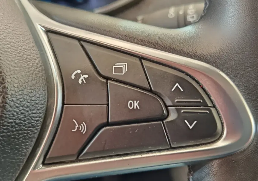 Gros plan sur les commandes multifonctions en plastique noir et contour argenté du volant cuir synthétique d'une Renault ZOE blanche.