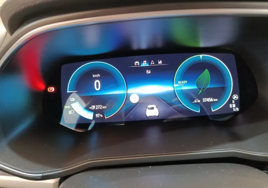 Gros plan sur le combiné d'instruments numérique de la Renault ZOE blanc, affichant vitesse, autonomie et état de charge.